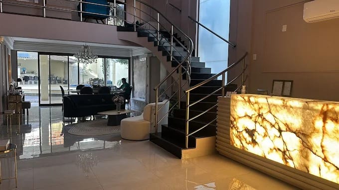 Recepção da clínica com balcão de ônix iluminado, escada de mármore escuro e sala de estar ao fundo